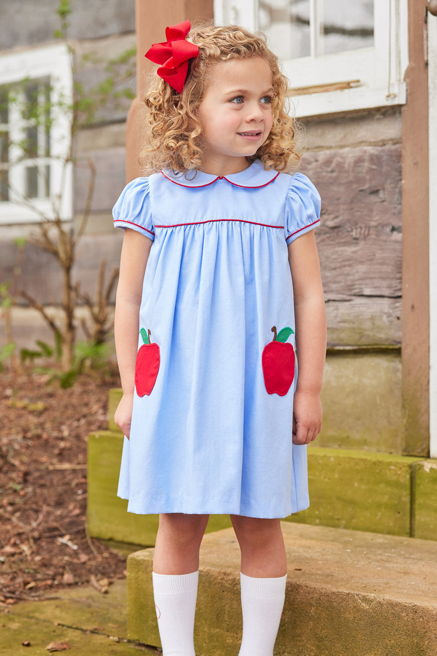 Little English traditional children's clothing. Light blue chambray dress for toddler girl . Back to school dress with red apple applique and red piping for fall.