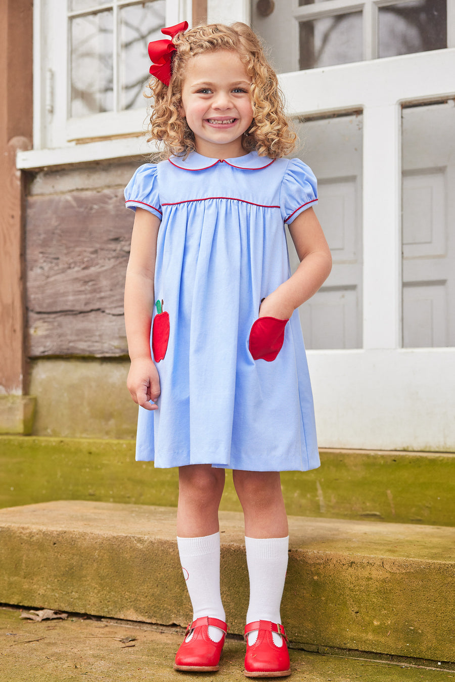 Little English traditional children's clothing. Light blue chambray dress for toddler girl . Back to school dress with red apple applique and red piping for fall. Paired with our apple knee high socks.