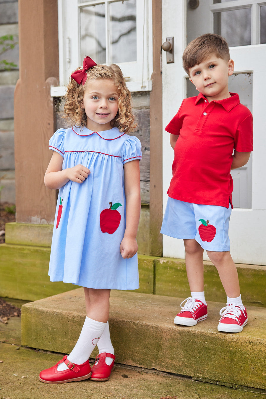 Little English traditional children's clothing. Light blue chambray dress for toddler girl . Back to school dress with red apple applique and red piping for fall. Paired with our apple knee high socks.