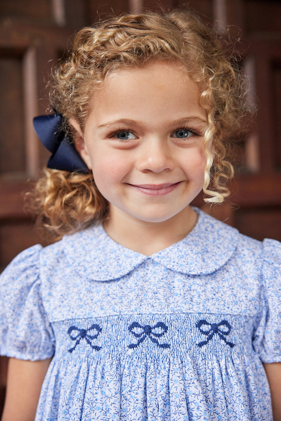 Little English traditional children's clothing. Classic smockked blue floral peter pan dress with navy bows for little girl for Fall